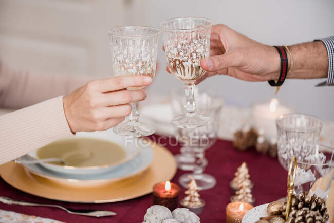 Crop unrecognizable couple with decorative glasses of alcoholic drink above served table with burning candles on Christmas Day at home — Stock Photo