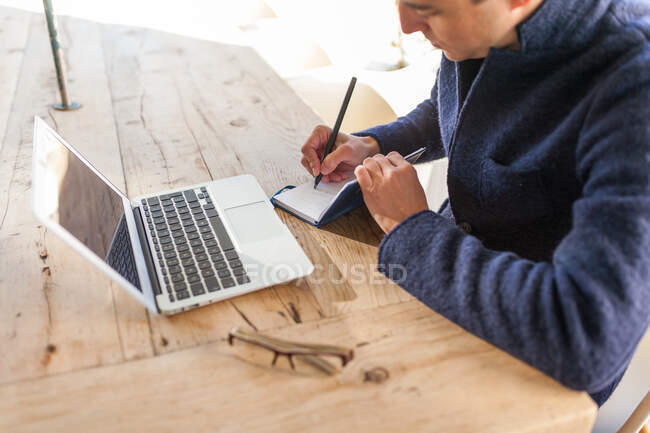 Seitenansicht eines jungen bärtigen Freiberuflers in lässiger Kleidung und Brille, der mit Laptop und Smartphone am Tisch sitzt, während er im Outdoor-Café an einem Projekt arbeitet — Stockfoto