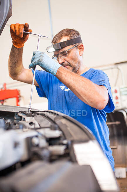 Mecánico masculino maduro enfocado con la llave que fija el automóvil moderno mientras que trabaja en servicio de reparación - foto de stock