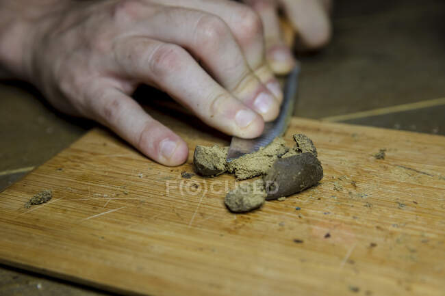 Врожай невизначений чоловік з ножем, що розмелює сушені шматочки рослини канабісу на дерев'яній дошці в робочому просторі — стокове фото