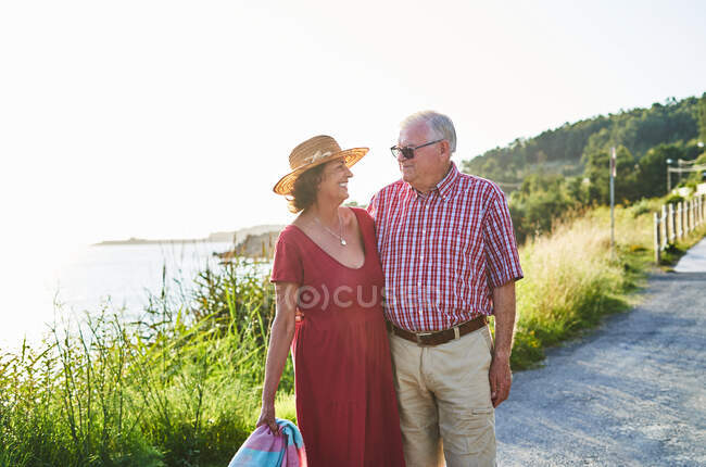 Старшая пара, стоящая рядом, глядя друг на друга и наслаждаясь видом на море в солнечный день — стоковое фото