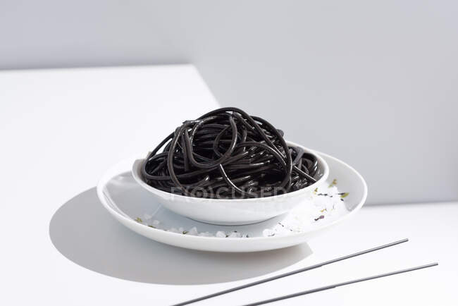 Du dessus du bol en céramique avec de délicieux spaghettis à l'encre de calmar noir avec des baguettes sur fond gris — Photo de stock