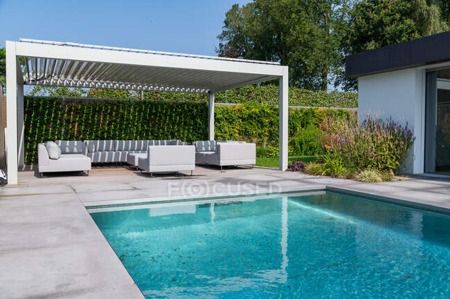 Hof einer teuren modernen Villa mit Schwimmbad und Lounge-Zone mit bequemen Sofas und Sesseln unter blauem Himmel — Stockfoto