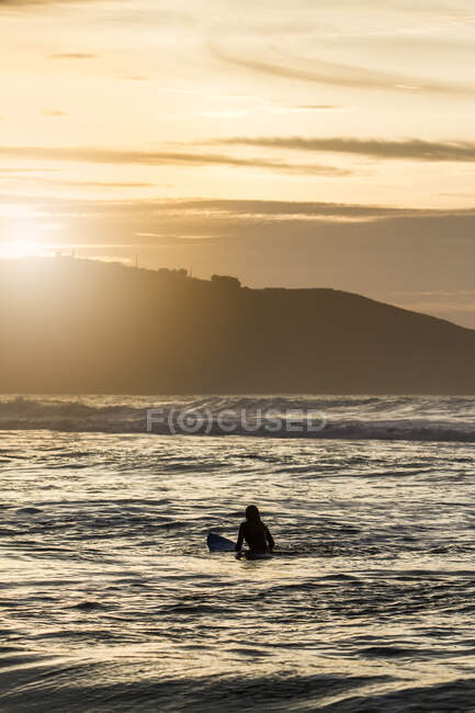 Visão traseira da jovem com prancha de surf no mar durante o pôr do sol na praia em Astúrias, Espanha — Fotografia de Stock