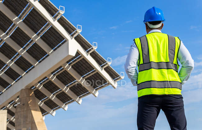 Low angle back view of unrecognizable male inspector in vest with protective helmet against modern solar power station — Stock Photo