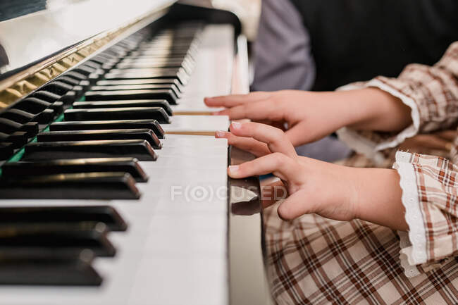 Cortar criança irreconhecível em vestido xadrez tocando piano, tendo tempo livre em casa em fundo turvo — Fotografia de Stock