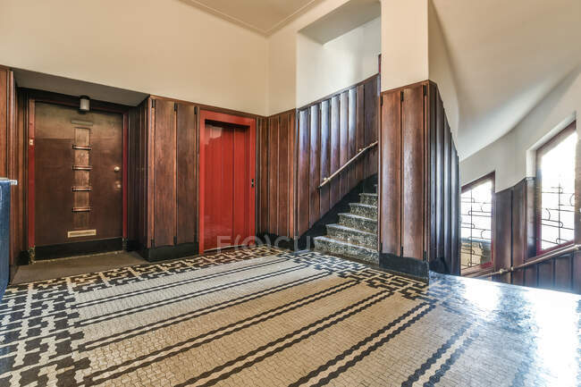 Interior de amplio hall con escalera con rejas y ascensor cerca de puerta a la luz del día - foto de stock