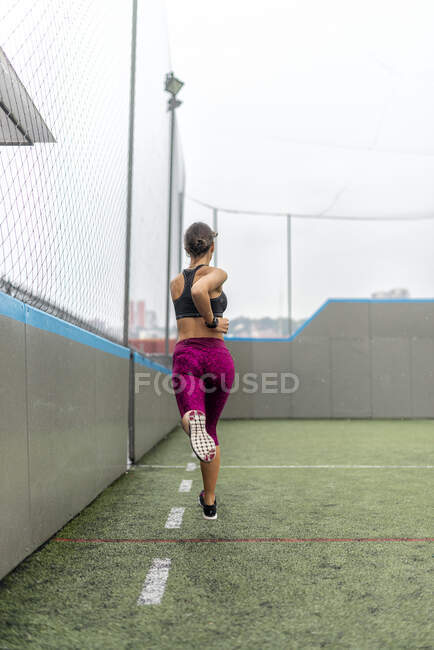 Full body of enduring female athlete in activewear running above ground during intense training in stadium — Stock Photo