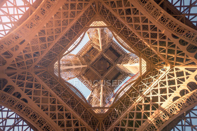 Desde abajo de la torre de observación con postes de apoyo y decoración simétrica en el día soleado en París Francia - foto de stock
