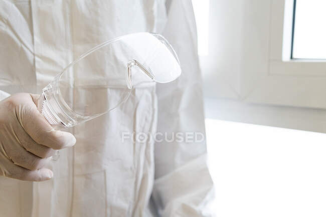 Médico macho irreconhecível cultivado em equipamento de proteção individual segurando óculos no hospital — Fotografia de Stock