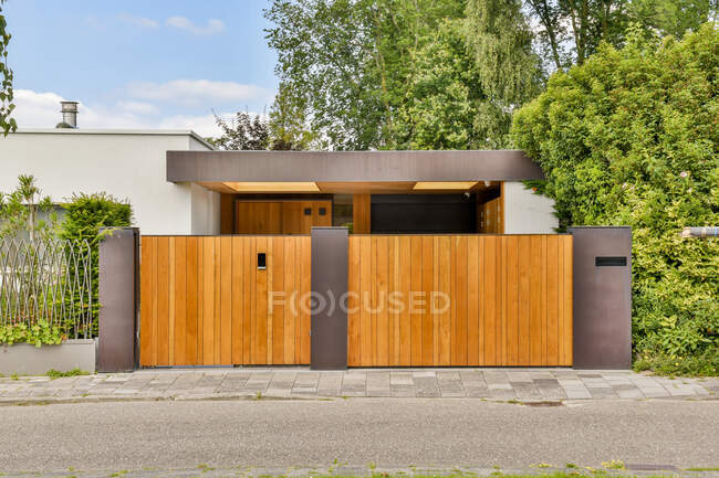Wooden gates of contemporary residential cottage with minimalist architecture surrounded by lush green trees on sunny day — Stock Photo
