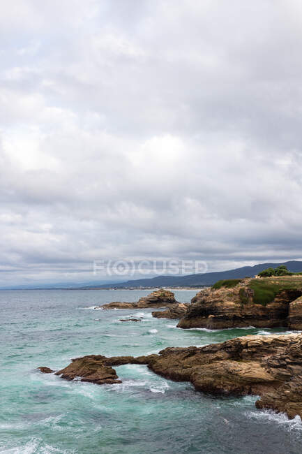 Spectacular view of wavy sea and rugged mounts under fluffy white clouds in stormy weather — Stock Photo