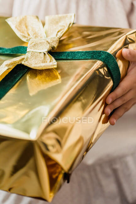 Crop unrecognizable child holding present box with golden wrapper and bow during New Year holiday — Stock Photo