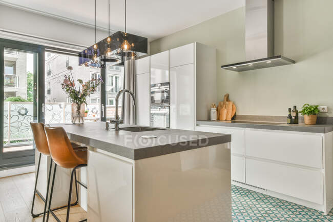 Interior elegante da cozinha moderna com armários e eletrodomésticos brancos e pia no balcão acima em casa grande com parede de vidro — Fotografia de Stock