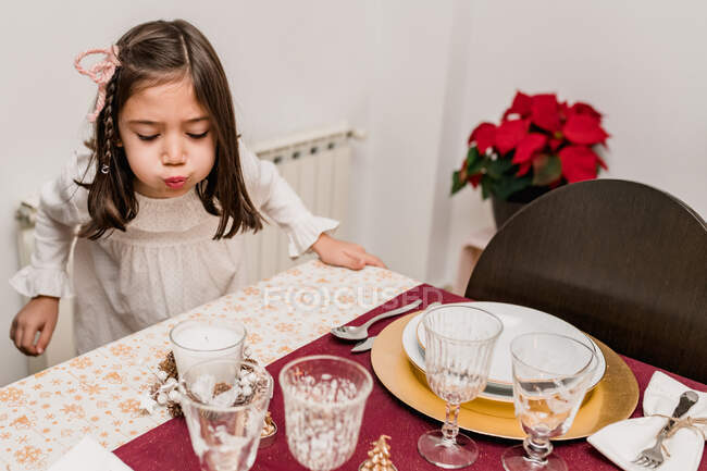 Cute girl in dress standing near festive table and blowing up candles during Christmas holiday celebration — Stock Photo