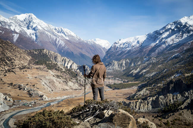 Rückansicht eines nicht wiederzuerkennenden Forschers mit fliegendem Haar, der am felsigen Hang steht und die malerische Landschaft der Bergkette in Nepal bewundert — Stockfoto