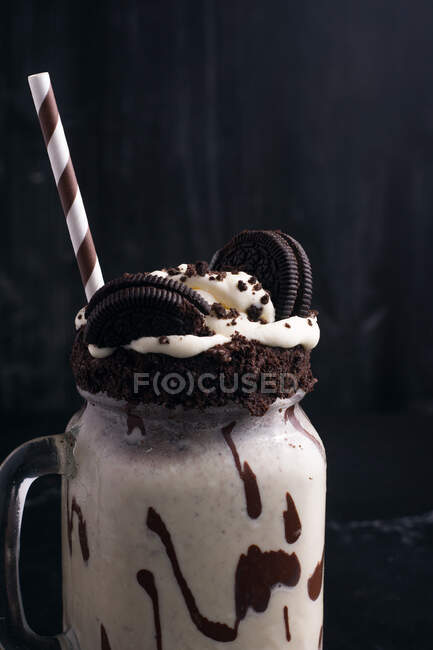 Tasty milkshake with crushed biscuits and straw in glass with chocolate sauce — Stock Photo