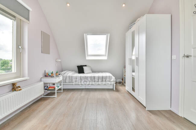Moderne Schlafzimmereinrichtung mit Bett und Schrank gegen Fenster über Spielzeug am Heizkörper zu Hause tagsüber — Stockfoto