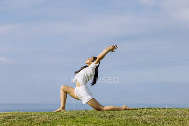 Сторона зору молодої етнічної жінки в спортивному лаві стоїть в позі Ашти Чандрасани під час практики йоги на березі моря. — стокове фото