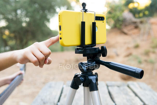 Cropped unrecognizable female teen guitarist recording video on modern cellphone on tripod in park on blurred background — Stock Photo