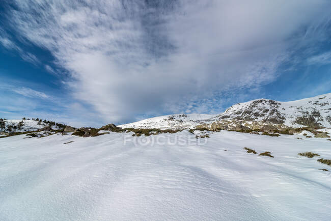 Мальовничий краєвид засніженої долини зі скелями, розташованими в високогір'ї в зимовий час під хмарним блакитним небом в денне світло — стокове фото