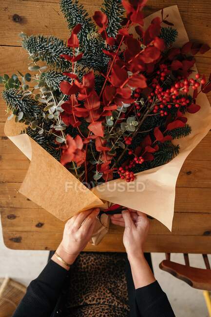 Зверху врожаю невпізнавана жінка-квітка, що стоїть за дерев'яним столом, влаштовуючи різдвяний букет в кімнаті — стокове фото