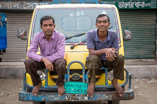 INDIA, BANGLADESH - DECEMBER 6, 2015: Ethnic barefoot males in shirt sitting on transport truck looking at camera — Stock Photo