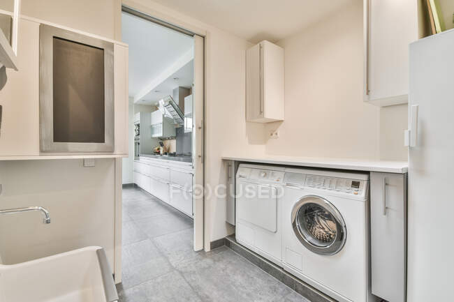 Lavatrice e asciugatrice contro pavimento piastrellato e lavabo in bagno contemporaneo in casa luce — Foto stock