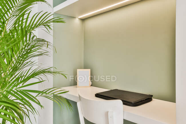 Intérieur du lieu de travail avec netbook sur pied sur la table sous la lumière dans une pièce minimaliste avec plante verte en pot — Photo de stock