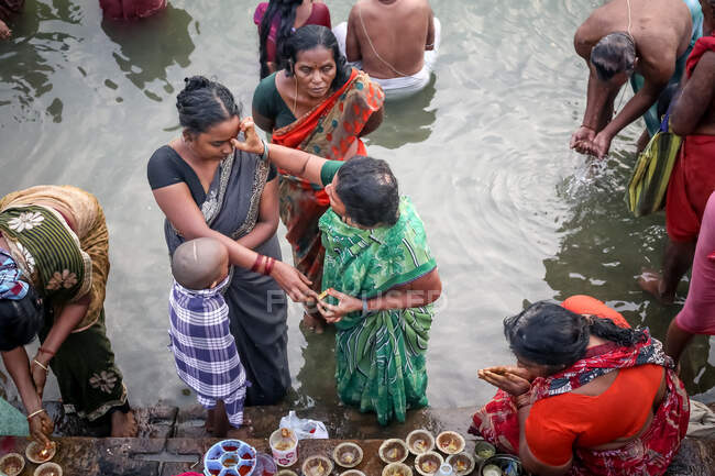 INDIEN, VARANASI - 2. NOVEMBER 2015: Von oben eine Gruppe ethnischer Frauen in traditionellen asiatischen Frauen in traditioneller indischer Kleidung, die beten und Opfergaben mit Kerzen und Blumen in Flussnähe in Indien darbringen — Stockfoto