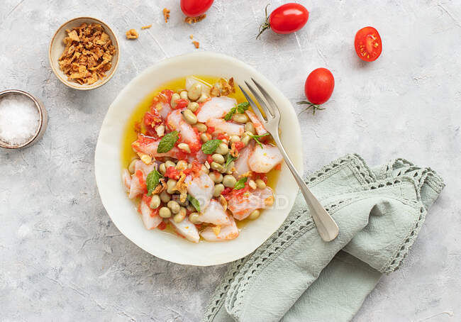 Ensalada de tomate y bacalao con abundante aceite de oliva en un plato profundo con un tenedor y un tazón de cebolla frita - foto de stock
