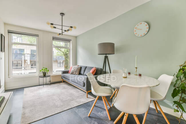 Sofá com almofadas entre mesa com planta em vaso e lâmpada no chão na sala contemporânea em casa durante o dia — Fotografia de Stock
