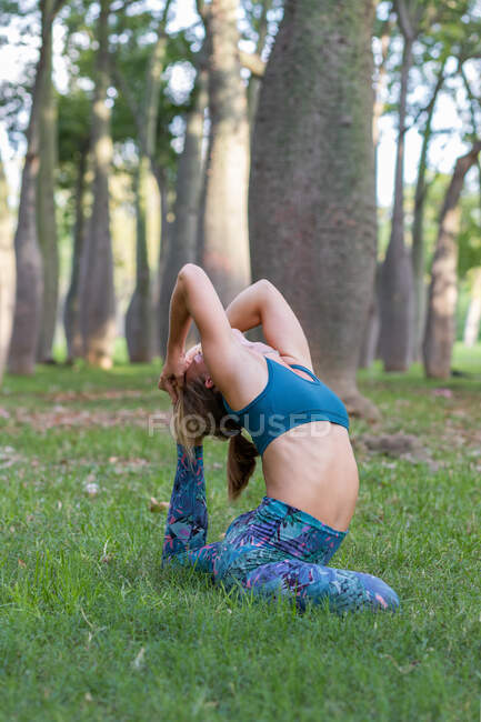 Vista lateral da fêmea flexível irreconhecível em sportswear realizando Eka Pada Rajakapotasana na grama verde na natureza durante o dia — Fotografia de Stock