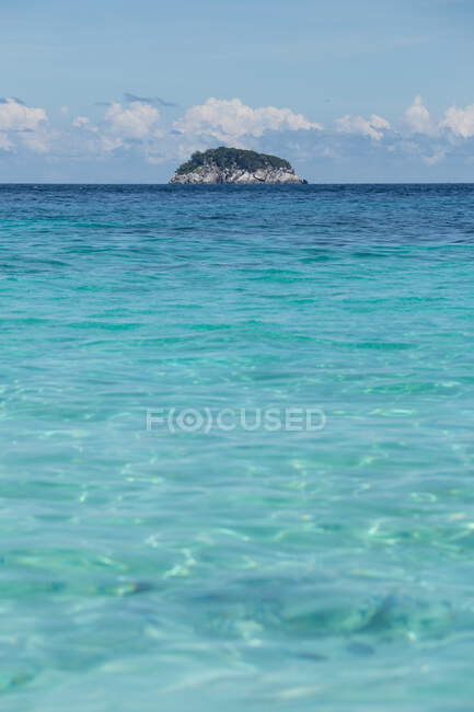 Пейзаж прозрачного синего волнистого моря с скалистым островом на горизонте под облаками в солнечный день в Малайзии — стоковое фото
