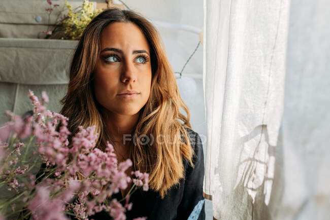 Retrato de una hermosa adolescente en casa mirando hacia otro lado rodeada de plantas - foto de stock