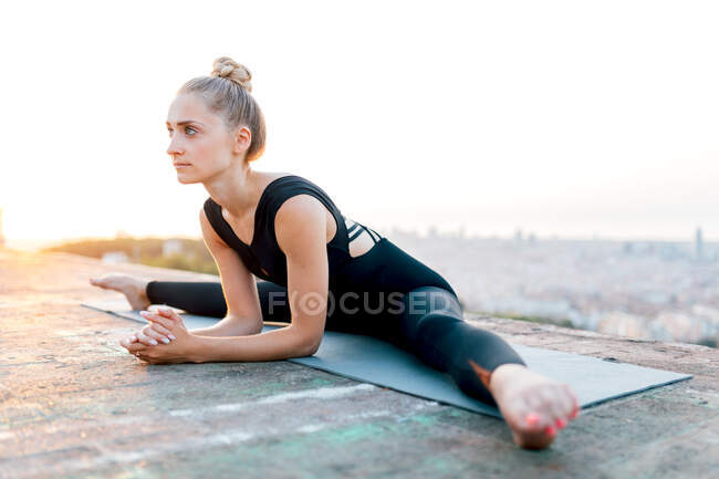 Full body of concentrated young female practicing Upavishta Konasana during outdoor yoga session on rooftop at sunset — Stock Photo