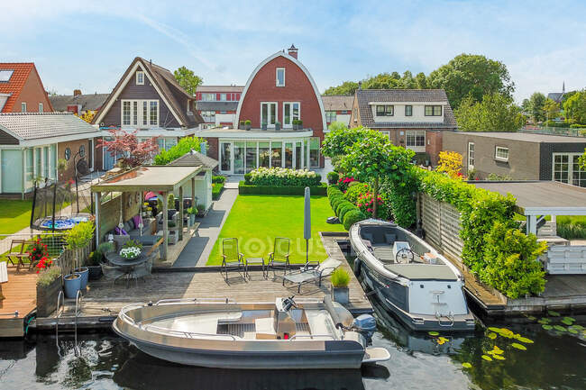 Barcos a motor amarrados en el río entre fachadas de edificios residenciales y plantas bajo el cielo nublado en la provincia de Utrecht Holanda - foto de stock
