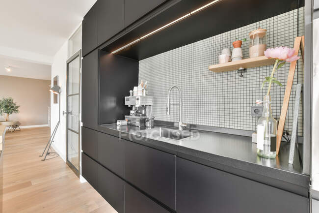 Machine à café moderne placée sur le comptoir de cuisine sombre près de l'évier dans la cuisine moderne avec armoires noires dans l'appartement en journée — Photo de stock