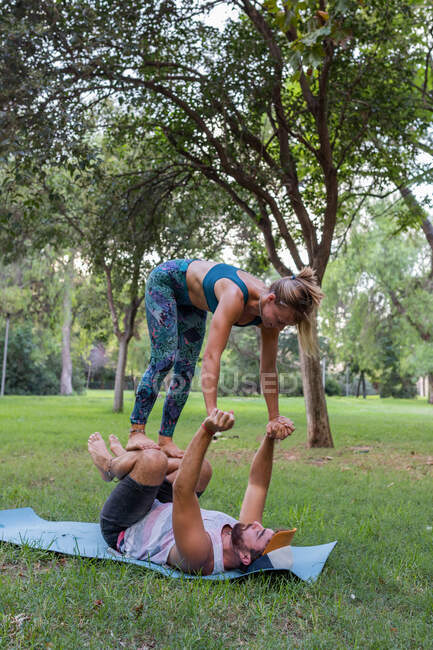 Duración completa de la pareja concentrada en ropa deportiva haciendo asana mientras practican acroyoga juntos en el parque verde a la luz del día - foto de stock