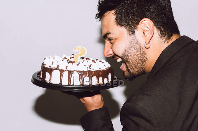 Vista lateral do macho alegre com a boca aberta segurando delicioso bolo de aniversário durante a festa — Fotografia de Stock