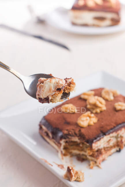 Високий кут врожаю ложки, що тримає смачний десерт тірамісу, прикрашений волоськими горіхами, який подають на білому столі — стокове фото