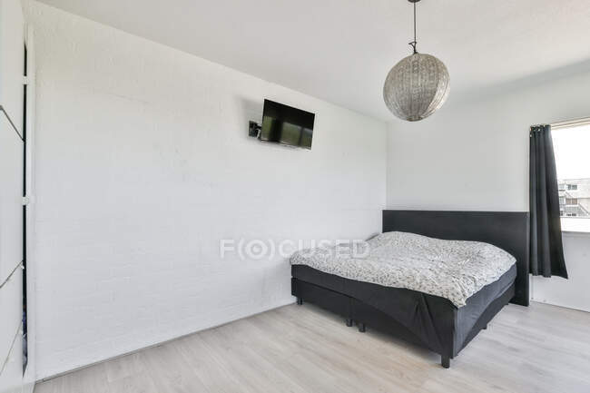 Чорне ліжко і телевізор в сучасній спальні з білими стінами в квартирі, спроектованій в мінімальному стилі — стокове фото