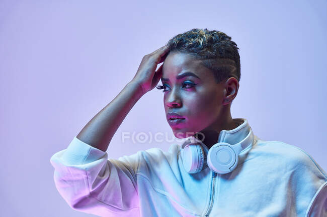 Thoughtful ethnic woman in trendy clothes with wireless headphones around neck looking away — Stock Photo