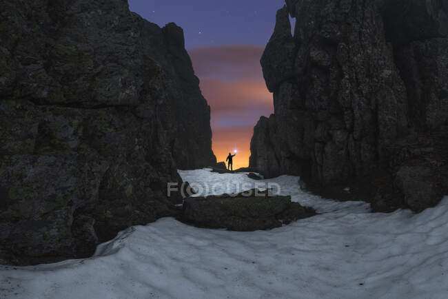 Турист з факелом на піщаній землі між грубими горами під хмарним небом з зірками на заході сонця — стокове фото