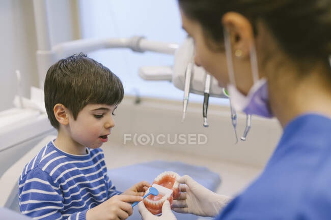 Ortodontista sorridente feminino ensinando paciente com escova de dentes a escovar dentes no modelo de mandíbula na clínica odontológica — Fotografia de Stock