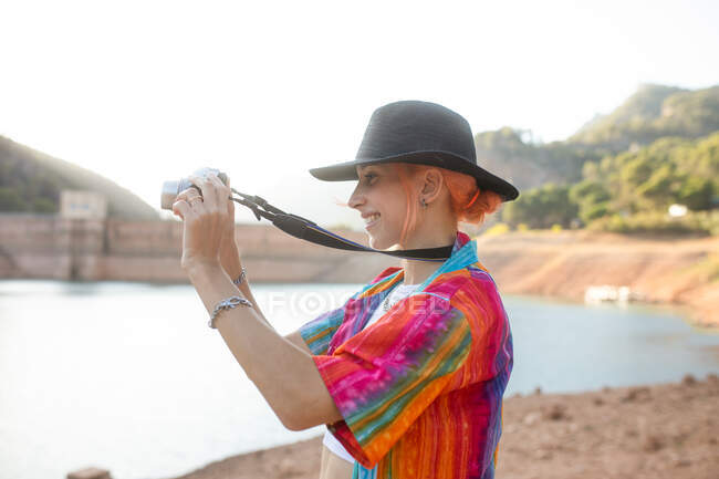 Mulher com chapéu preto em um lago tirando fotos da paisagem — Fotografia de Stock
