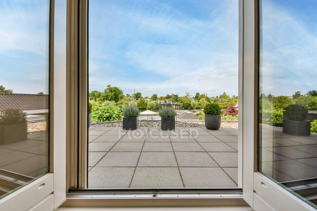 Porta contra plantas em vasos na varanda sob céu azul nublado no dia de verão na luz solar — Fotografia de Stock