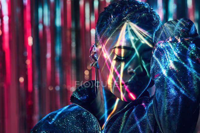 Young African American female with closed eyes standing in ultraviolet light on blurred background — Stock Photo