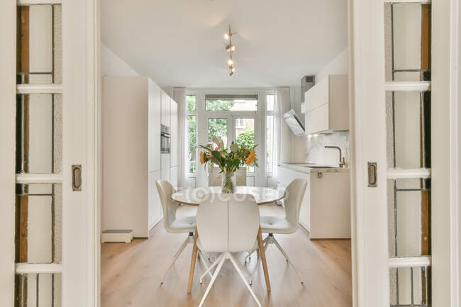 Tavola rotonda con mazzo di fiori posizionato vicino alla cucina luminosa in appartamento moderno durante il giorno — Foto stock