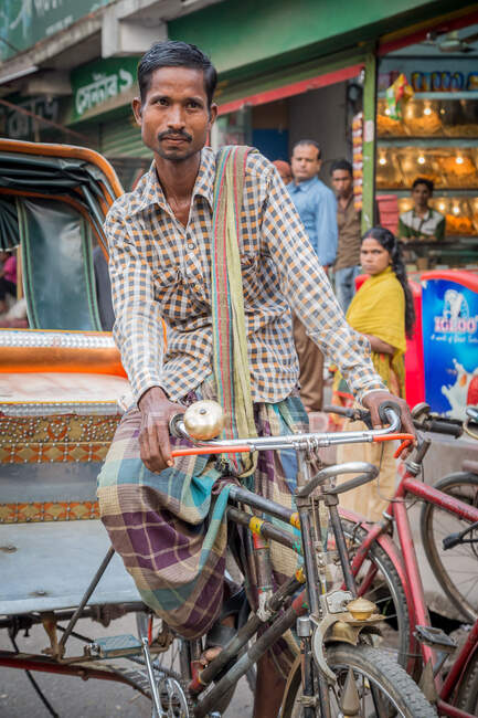 INDIA, BANGLADESH - 6 DE DICIEMBRE DE 2015: Varón étnico sentado en triciclo en la calle de la ciudad mirando hacia otro lado - foto de stock